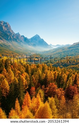 Seasonal autumnal scenery in Dolomite Alps, Cortina d'Ampezzo, Italy. Sunny day with yellow larches below and valley covered by fog and high mountains behind. Popular travel destination in autumn