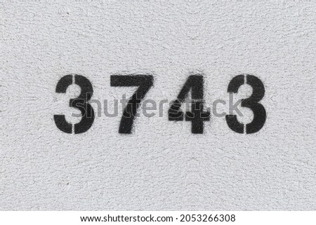 Black Number 3743 on the white wall. Spray paint. Number three thousand seven hundred and forty three.