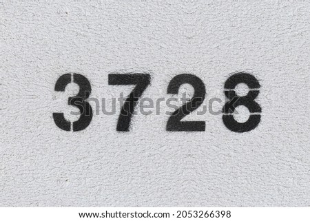 Black Number 3728 on the white wall. Spray paint. Number three thousand seven hundred and twenty eight.