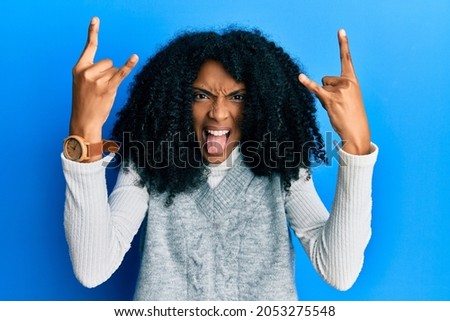 African american woman with afro hair wearing casual winter sweater shouting with crazy expression doing rock symbol with hands up. music star. heavy music concept. 