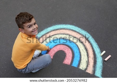 Happy child drawing rainbow with chalk on asphalt, above view