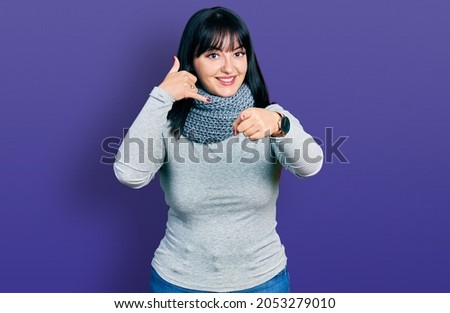 Young hispanic plus size woman wearing winter scarf smiling doing talking on the telephone gesture and pointing to you. call me. 