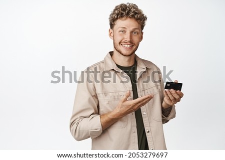 Handsome smiling man shows credit card, demonstrated bank announcement on copy space, stands against white background