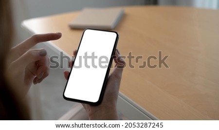 Mockup image blank white screen cell phone.women hand holding texting using mobile on desk at home office.

