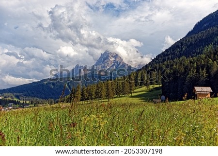 View of some cloud-covered peaks of the famous Sesto Dolomites behind a blooming meadow with an old wooden hut, Alps, South Tyrol, Italy, Europe