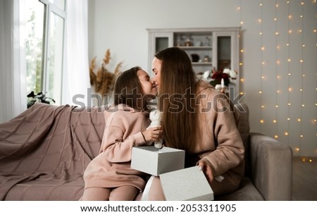 daughter and mom are sitting on the couch with an open gift and kissing