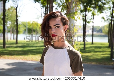 young latina woman is in a park where she is going to start doing her make-up for her big change from boy to girl. Concept of diversity, transgender, and freedom of homosexual expression. Royalty-Free Stock Photo #2053317410