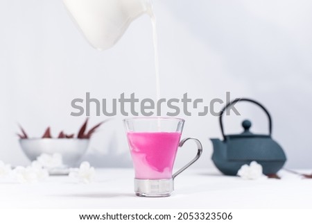 Pouring milk into a cup of berry tea on a white table and light gray background