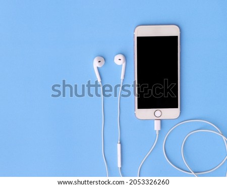 Smartphone connected to headphones on blue background, top view.