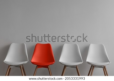 Three white chairs and red on gray wall background in office or room. Row of stools with one of different colour. Job opportunity, recruitment, business, leadership and hiring concept, copy space Royalty-Free Stock Photo #2053331993