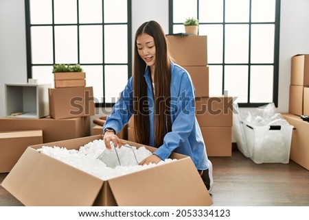 Young chinese girl smiling happy unboxing cardboard package at new home