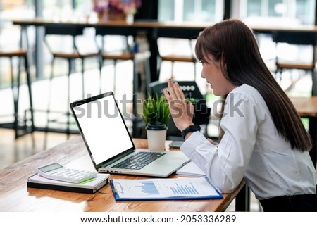 Image of young Asian businesswoman having an online meeting using a laptop blank white screen with a calculator document put on the office desk.