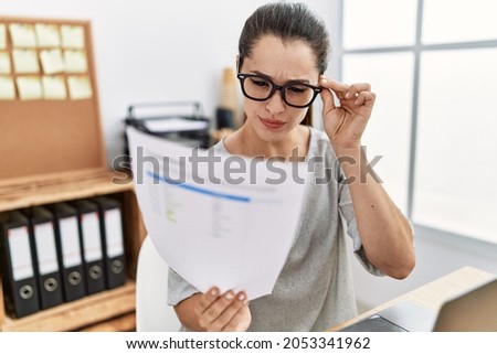 Young hispanic woman with serious expression reading document at office