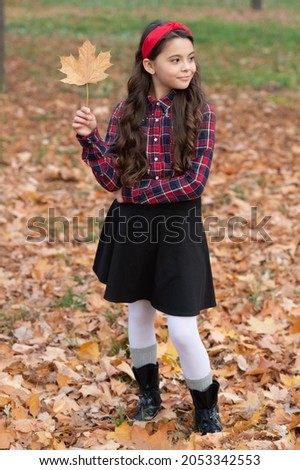 cheerful kid in school uniform hold autumn maple leaf outdoor, fall