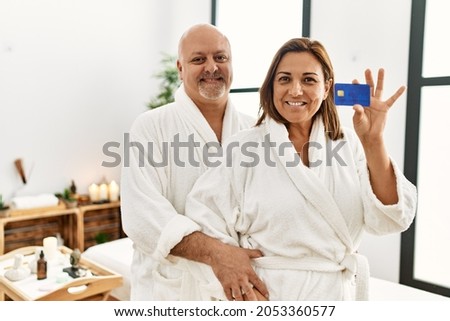 Middle age hispanic couple smiling happy and  holding credit card at beauty center.