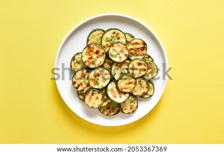 Roasted zucchini on plate over yellow background. Top view, flat lay Royalty-Free Stock Photo #2053367369