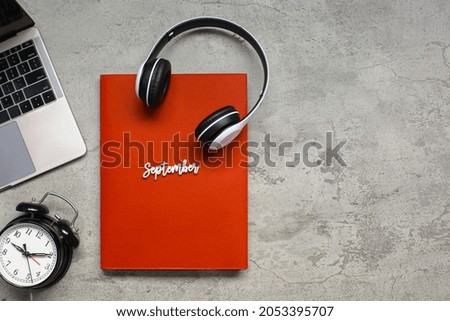 Month of September creative flat lay composition with red book and multimedia entertainment accessories on grey cement background