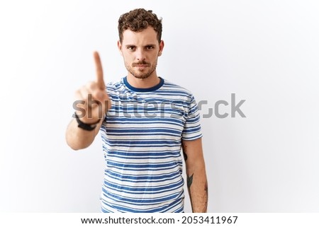 Handsome young man standing over isolated background pointing with finger up and angry expression, showing no gesture 