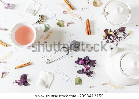 Tea time femine composition with tea pot, cinnamon, cup, tea strainer, purple and pink leaves and dried plants  on white background. Flat lay, top view. 