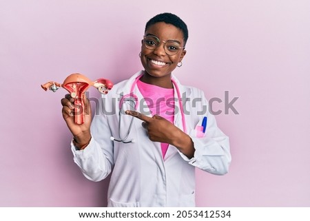 Young african american doctor woman holding anatomical model of female genital organ smiling happy pointing with hand and finger  Royalty-Free Stock Photo #2053412534