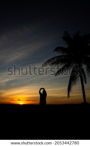 Silhouette of an adult man taking a picture with a cell phone during a beautiful sunset in the tropics. Holiday landscape.