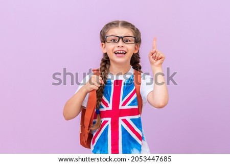 A schoolgirl with an image of the English flag on a T-shirt with glasses points her finger at the top. Learning English. isolated background.