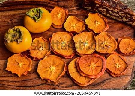fresh ripe whole Japanese persimmons along with slices of the dried fruit Royalty-Free Stock Photo #2053459391