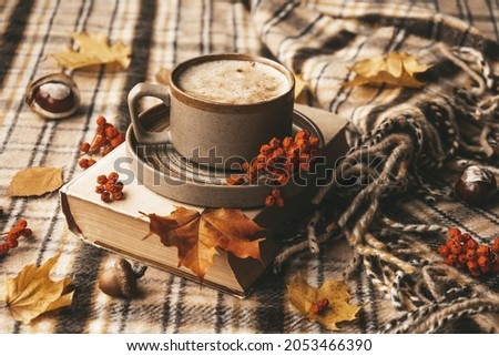 Atmospheric cozy autumn composition. Hot mug of coffee, book, fall leaves, chestnut, ashberry, acorns and cozy brown plaid as background. Sunday loneliness relaxing, hugge mood. Thanksgiving day. Royalty-Free Stock Photo #2053466390