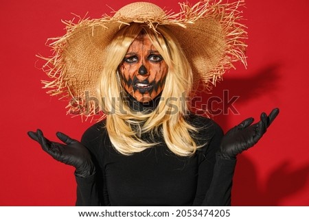 Young displeased sad woman with Halloween makeup mask wears straw hat black scarecrow costume spread hands ask why isolated on plain red background studio portrait. Celebration holiday party concept