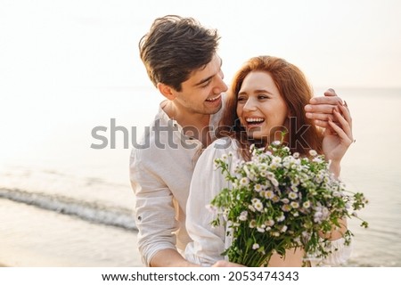Young fun surprised couple family man woman in white clothes rest relax together boyfriend meet girlfriend close eyes gift give bouquet flowers at sunrise over sea beach outdoor seaside in summer day Royalty-Free Stock Photo #2053474343