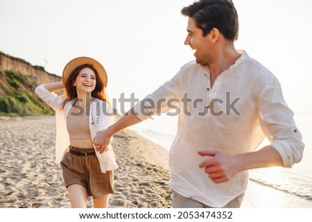 Excited lovely young couple two friends family man woman in white clothes hold hands running walk stroll dance together at sunrise over sea beach ocean outdoor seaside in summer day sunset evening. Royalty-Free Stock Photo #2053474352