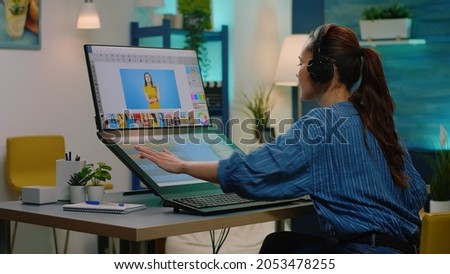 Retouch artist working with editing software on touch screen for photography project at studio. Photographer wearing headphones while retouching photos using technology and devices