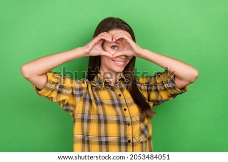 Portrait of funny lovely person hands make heart symbol eye peek toothy smile isolated on green color background
