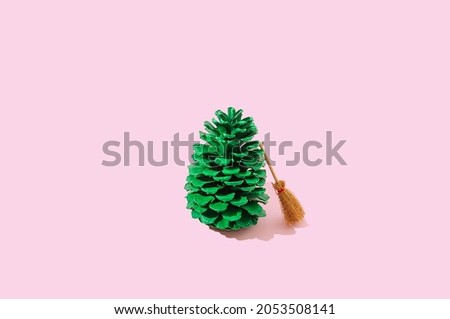 A broom leaning on a green pine cone. Pastel pink background. Minimal Autumn creative design. Winter is coming after fall artistic concept.