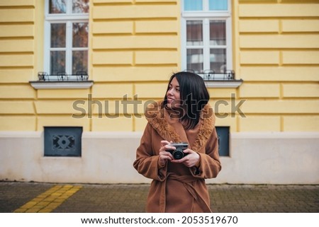 Young hispanic woman using a retro camera while out in the city wearing coat