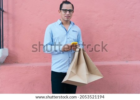 Man standing with shopping bags in front of a pink wall