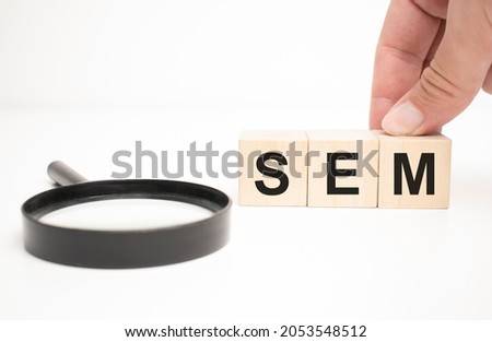 sem text wooden cube blocks and hand holding magnifying glass on table background.
