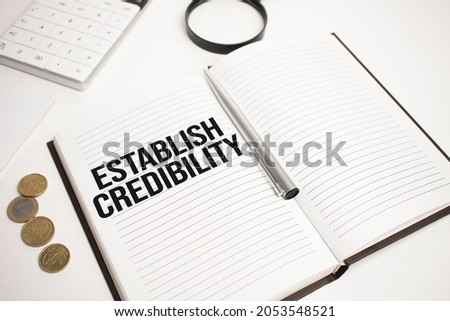 Business accessories, calculator, coins, reports and magnifier glass with text ESTABLISH CREDIBILITY