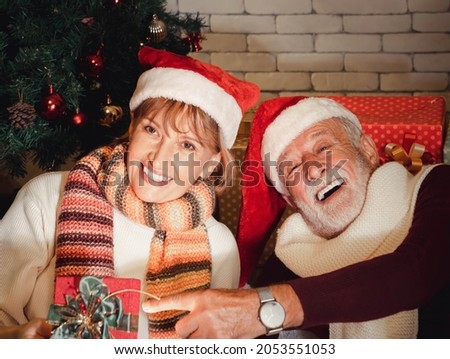 closeup portrait of happy senior Caucasian couple with Santa Claus hat holding Christmas gift celebrate together at home. warm and romantic winter holiday.