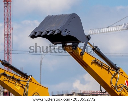 Lifted bucket of new excavator against the background of the construction site. Close-up of new construction equipment