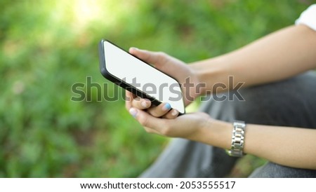 Side view, Female sits at a park and hold mobile phone. phone blank screen mockup for montage your graphic