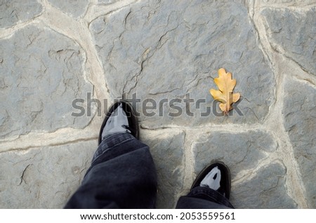 Photo of feet in shoes on the ground with a fallen yellow oak leaf in autumn in the park
