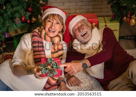 caucasian senior couple feel happy giving present and celebrate Christmas night together with decorated Christmas tree at home