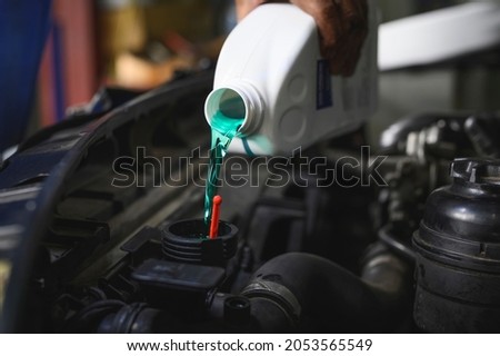 Auto mechanic filling Pre-mixed Super Long Life Coolant fluid in car radiator fill hole. Royalty-Free Stock Photo #2053565549