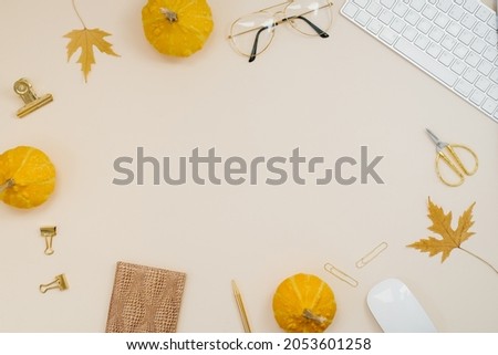 Flat lay home office desk. Freelancer or blogger workplace with computer, yellow pumpkins, fallen leaves, glasses, notepad and pen on a light beige background with copy space. Autumn composition