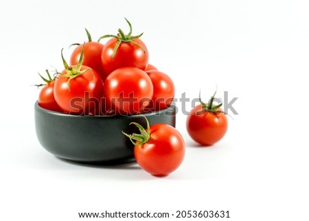 Red tomatoes in a black ceramic cup and placed on a white floor.