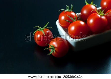 Delicious red tomatoes are housed in white ceramic vessels and placed on a black floor, selective focus.