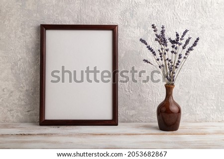 Brown wooden frame mockup with lavender in ceramic vase on gray concrete background. Blank, vertical orientation, still life, copy space.