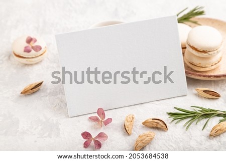 White business card mockup with cup of coffee, almonds and macaroons on gray concrete background. Blank, side view, still life.