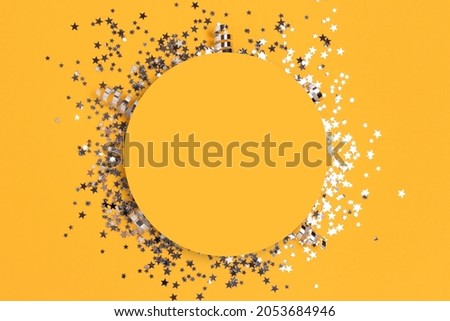 Round frame made of silver colored confetti on a yellow background. 